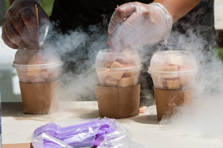 Man's hands prepare frozen deserts using liquid nitrogen at ice cream festival. 