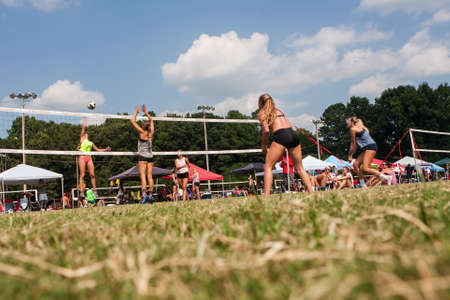 Doraville, GA, USA - August 25, 2018:  Low-angle wide shot shows female volleyball players competing in a triples grass volleyball tournament at Honeysuckle Park on August 25, 2018 in Doraville, GA.のeditorial素材