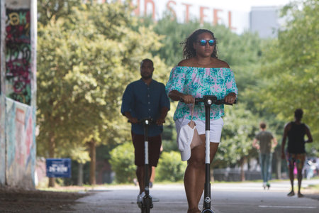 Atlanta, GA, USA - July 6, 2019:  A couple ride motorized scooters under a bridge along the Atlanta...