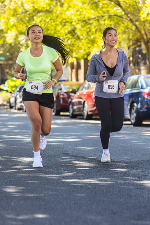 Suwanee, GA / USA - October 15, 2022:  Two young Asian American women run down residential street as...