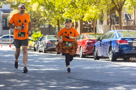 Suwanee, GA / USA - October 15, 2022:  A couple wearing pumpkin shirts run down a residential street as they near the finish line of the Spooky Spirits 5K, on October 15, 2022 in Suwanee, GA.のeditorial素材