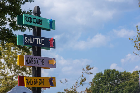 Painted wooden signs on a pole give info and directions with arrows at a fall festival.