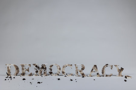Wood letters spell out the word democracy against a white seamless background. The letters are burned and muddied.の写真素材
