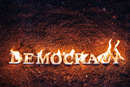 Wood letters spelling out the word democracy are lit on fire at night.の写真素材