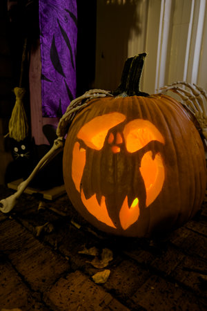 A pumpkin carved with an image of a ghost glows with an orange candle as part of a home's Halloween decorations.の写真素材