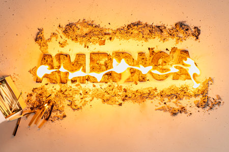 Wooden letters spelling the word "America" burn against a white seamless background, with a lit match from a matchbox sitting nearby.の写真素材
