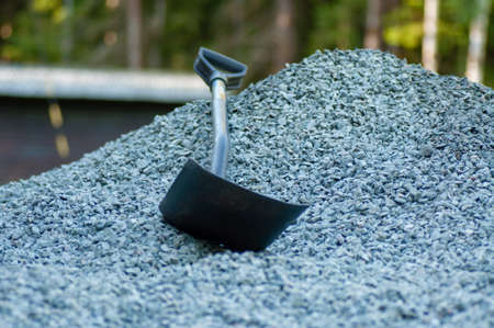 a chovel in a pile of grey gravel infront of a forestの写真素材