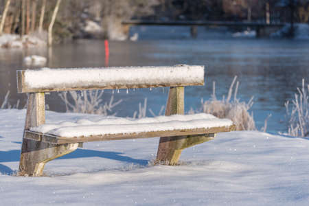 a cold and frozen bench covered in snow in swedenの写真素材