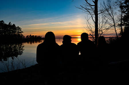 family of four looking at the sunset over a lakeの写真素材