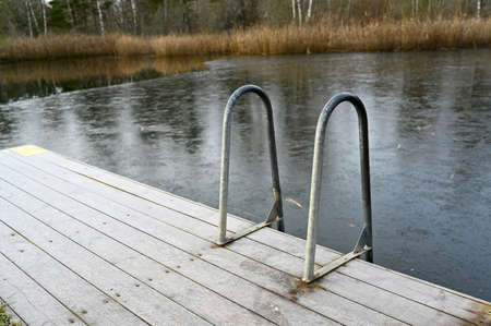 wooden jetty with bathing ladder on frozen lakeの写真素材