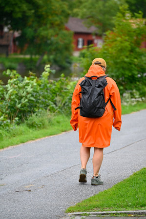 Person walking in a orange raincoat near Black river Orebro Swedenの写真素材