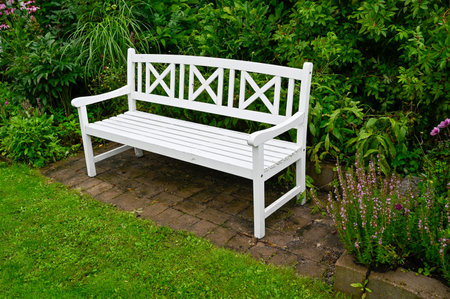 Wooden park bench painted white standing in green gardenの写真素材