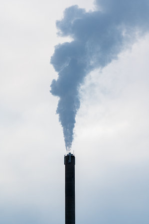 High chimney with pillar of smoke against grey skyの写真素材