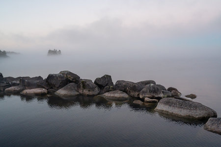 Calm water with stones and small island in mistの写真素材
