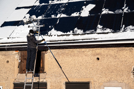 Man removing snow from solar panels on roofの写真素材
