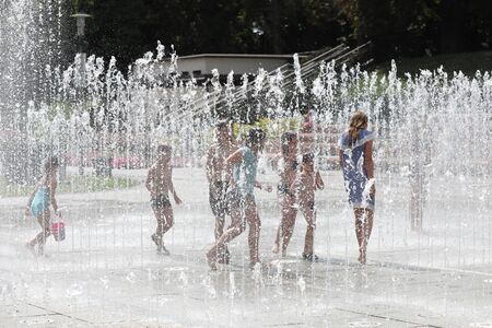 A cheerful child playing in the fountain and enjoying the cool streams of water on a hot summer dayの写真素材