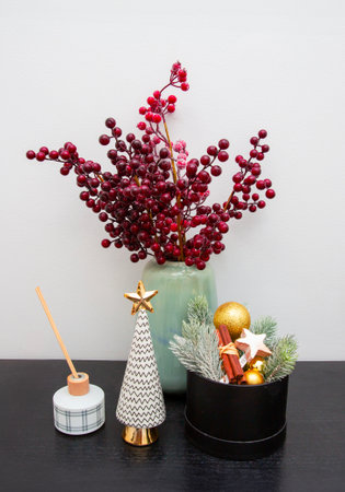 Vase with red berries and Christmas decorations against a white wall.