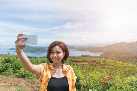 Female traveler selfie with her smart phone and beautiful landscape at kanchanaburi thailandの写真素材