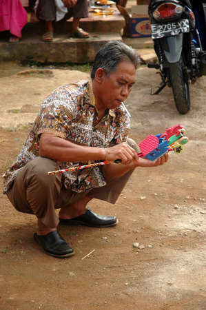 cikijing, west java, indonesia - july 10, 2011  old man holding toy and get smokingのeditorial素材