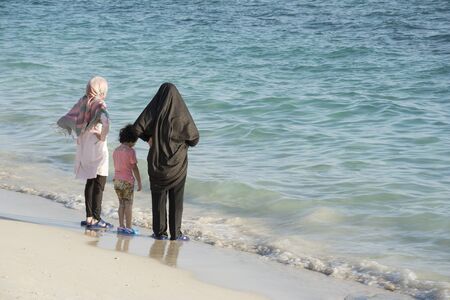 A Mother with Her Two Girls Contemplating on The Beach, Looking and Enjoying From Coming Waves.の写真素材