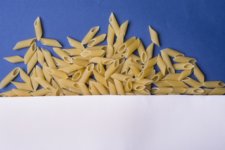 White paper covered tubular penne pasta on blue background. Food background texture, Top viewの写真素材