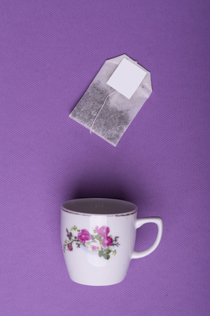 Single porcelain white cup with single tea bag on purple background. top view studio shotの写真素材