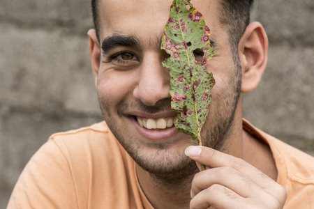 Happy young man holding a ruin leaf in front of face at outdoor areaの写真素材