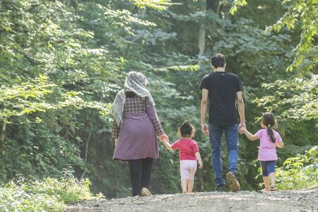 Backside of young family walking together outside in green nature, travel and spending holiday time concept の写真素材