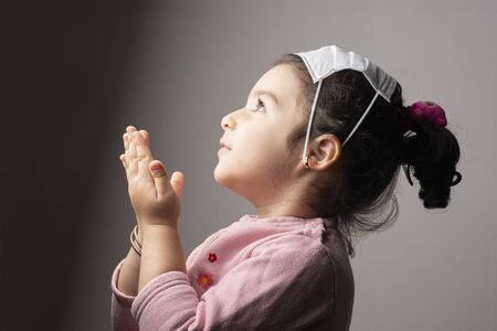 Praying Little girl wearing mask on her head in front of epidemic coronavirus outbreak, science vs...