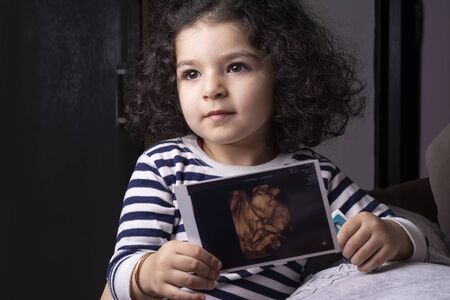 A two years old girl holding her unborn baby sonography image in handsの写真素材
