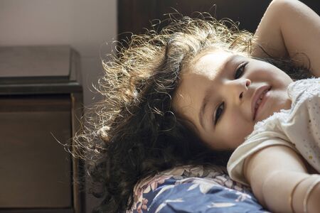 Beautiful morning sunlight coming in form bedroom window and lighten little girl hairの写真素材
