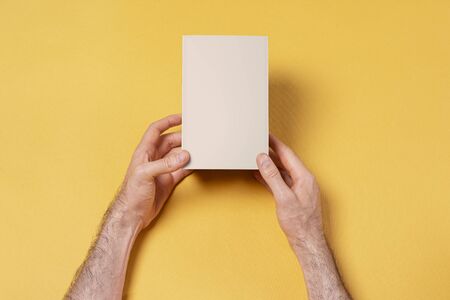 Male hands holding a small box in front of yellow background, mock-up series template ready for your design, face selection path includedの写真素材