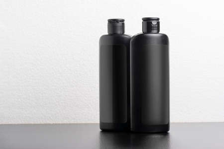 Black hair shampoo bottles in front of  light gray background, editable mock-up series template...