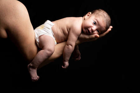 Two months years old little newborn baby resting on her motherâ€™s arm in front of dark...