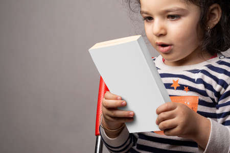 Little girl reading a novel book with blank cover in front of body, editable mock-up series template...
