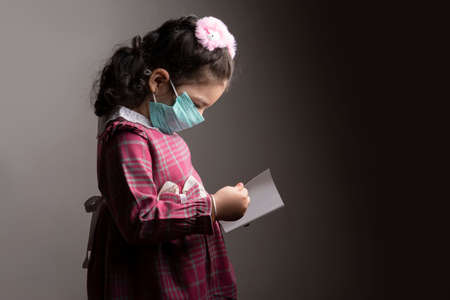 A little girl with protection hospital mask studying a book, Anonymity and virus protection conceptの写真素材