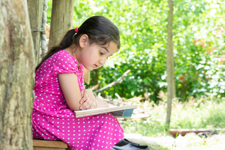 Young little girl sitting and reading a book in outside the houseの写真素材