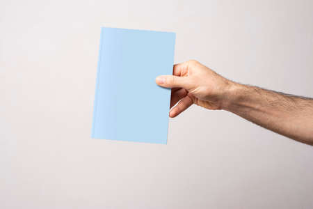 Male hand holding a closed book-catalog with blank cover, mock-up series template ready for your design, book cover selection path icluded.の写真素材