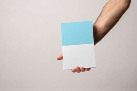 Male hand holding a closed book-catalog with blank cover, editable mock-up series template ready for your design, cover selection path included.の写真素材