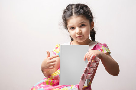 Little girl pointing a story book with blank cover sit on chair, editable mock-up series template ready for your design, cover selection path included.の写真素材