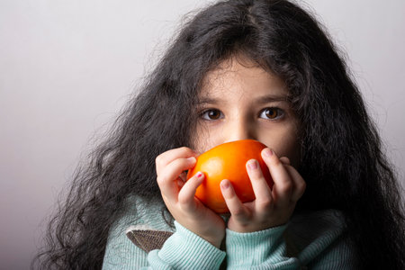 Little girl portrait holding a persimmon by hands in front of mouthの写真素材
