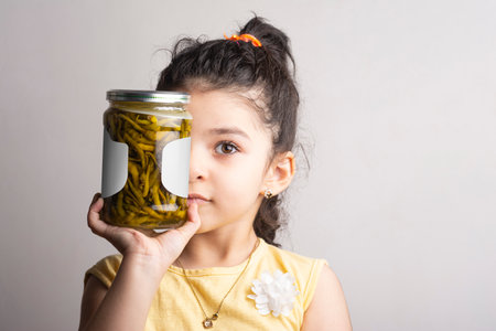Little girl holding a pickled pepper glass conserve in front of face, label selection path included.の写真素材