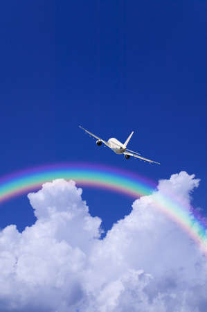 A jetliner aeroplane flying over white clouds towards a rainbow in blue skyの写真素材