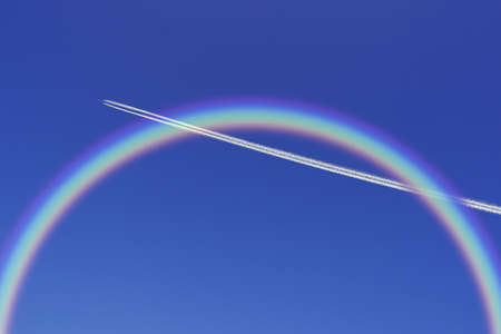 A jetliner aeroplane flying with rainbow in blue skyの写真素材