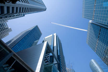 A view up through tall skyscrapers to a patch of blue sky with a jetliner flying overhead.のeditorial素材