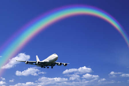A jetliner aeroplane flying over white clouds towards a rainbow in blue skyの写真素材
