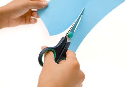 Hands holding a pair of scissora and cutting a piece of blue paper over whiteの写真素材