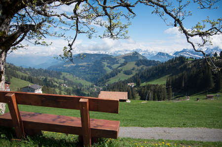 Brown wooden chair overlooking the swiss alps on mount rigi. Rest station with a view. Snow capped mountainsの写真素材