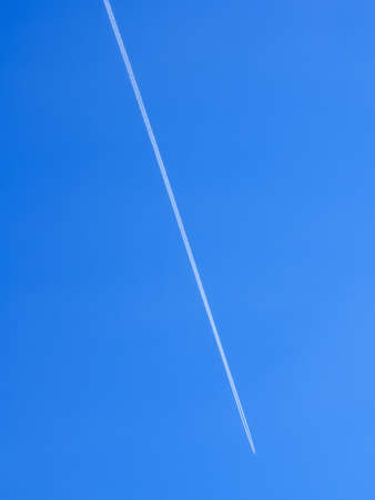 Airplane flight path in the clear blue sky leaving condensation (vapor) trails behindの写真素材