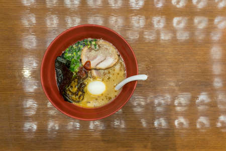 Red bowl of delicious tonkatsu (pork bone soup) ramen with egg, seaweeds and spring onion